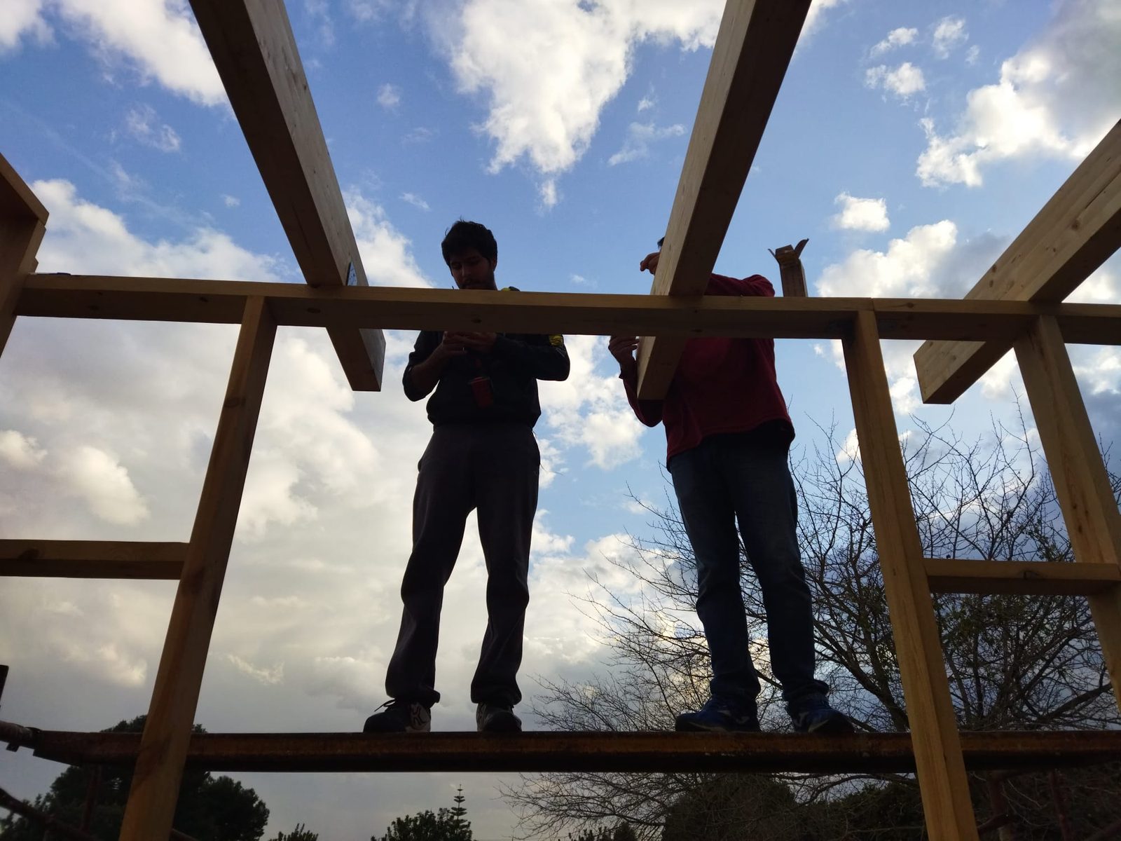 Manuel y su padre sobre la estructura, montando las vigas de la cubierta a contraluz